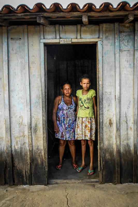 Maria Helena (esq) e a filha Railene (dir) posam na porta de sua casa. A menina sofre de diabetes e doenças respiratórias. Maria Helena deixou o emprego para cuidar da filha e vive do Bolsa Família. Mãe e filha vivem em um ambiente insalubre, com chão de terra batida e paredes de madeira apodrecida. Foto: Fabíola Ortiz/O Eco